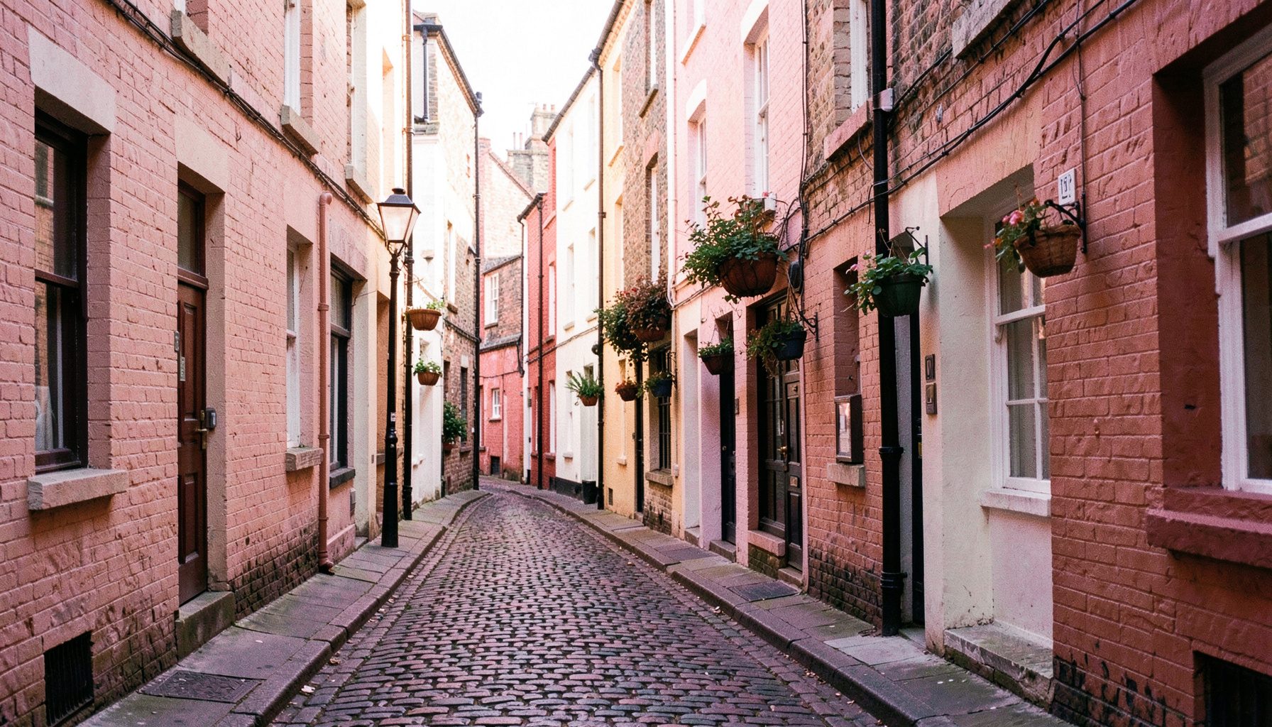 A narrow cobbled side street in an old Liverpool quarter, bathed in soft warm afternoon light — painted brick facades in muted tones.