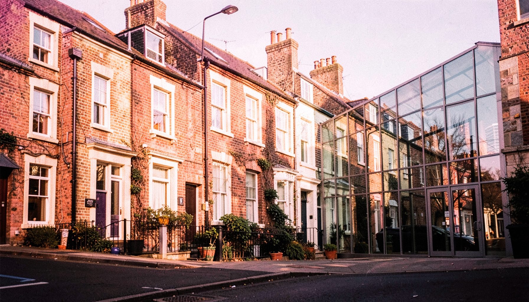 A row of Georgian terraced houses alongside a modern glass gallery, both bathed in warm afternoon light — a candid streetscape of Liverpool.
