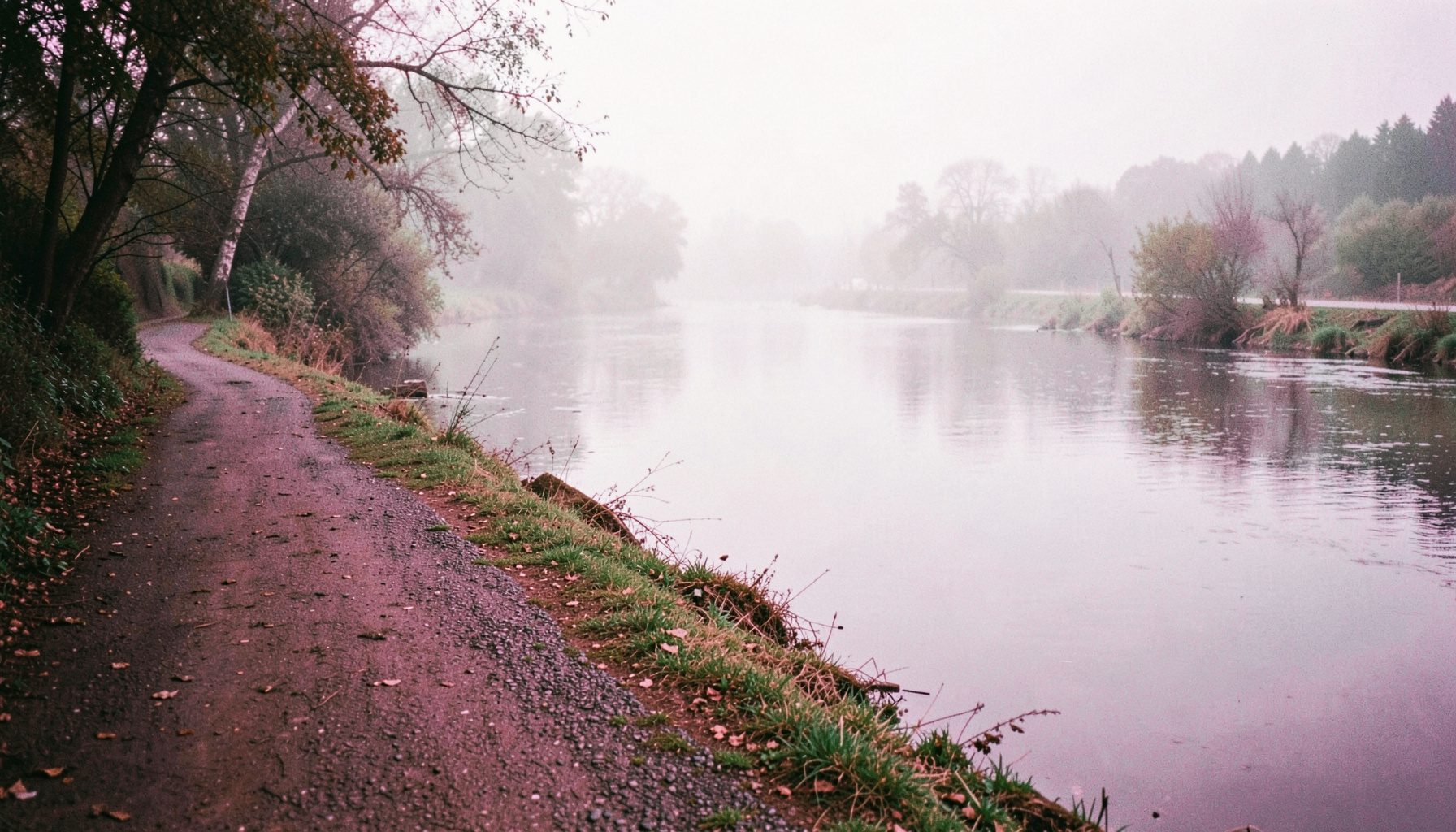 A quiet riverside path on a misty morning, with pale greys and soft pinks reflected in the still water — a candid, observational photograph of the Liverpool waterfront.
